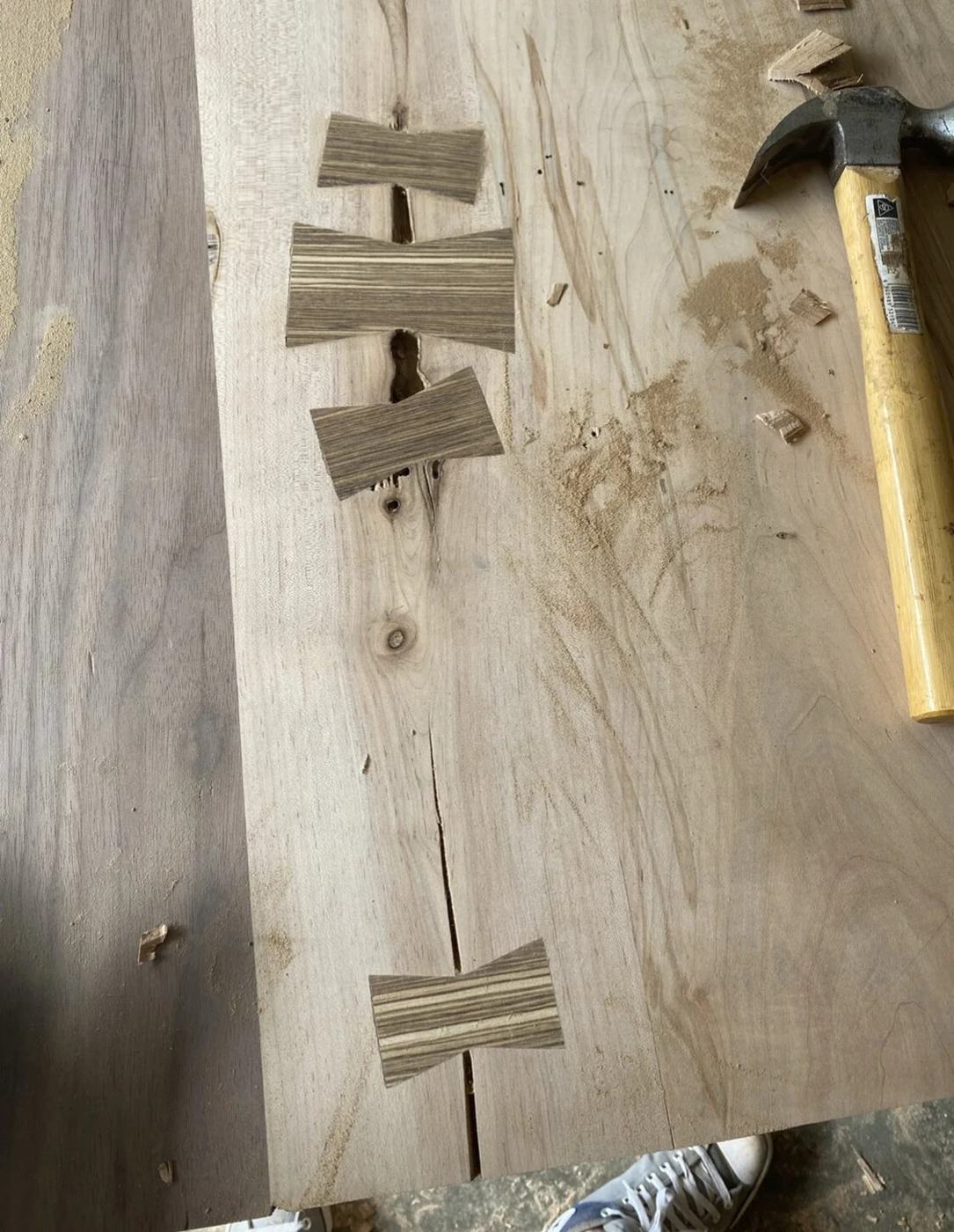 Contrasting butterfly keys inlaid across a crack in a light hardwood slab, with a mallet nearby
