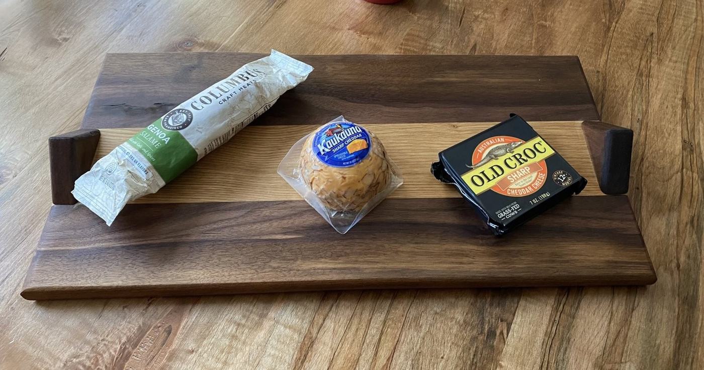 Walnut serving board with handles holding cheese and salami
