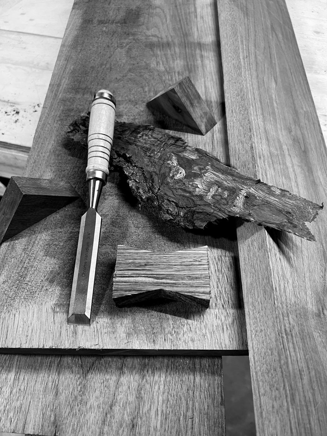 Black and white photo of a chisel resting on walnut boards next to two butterfly keys