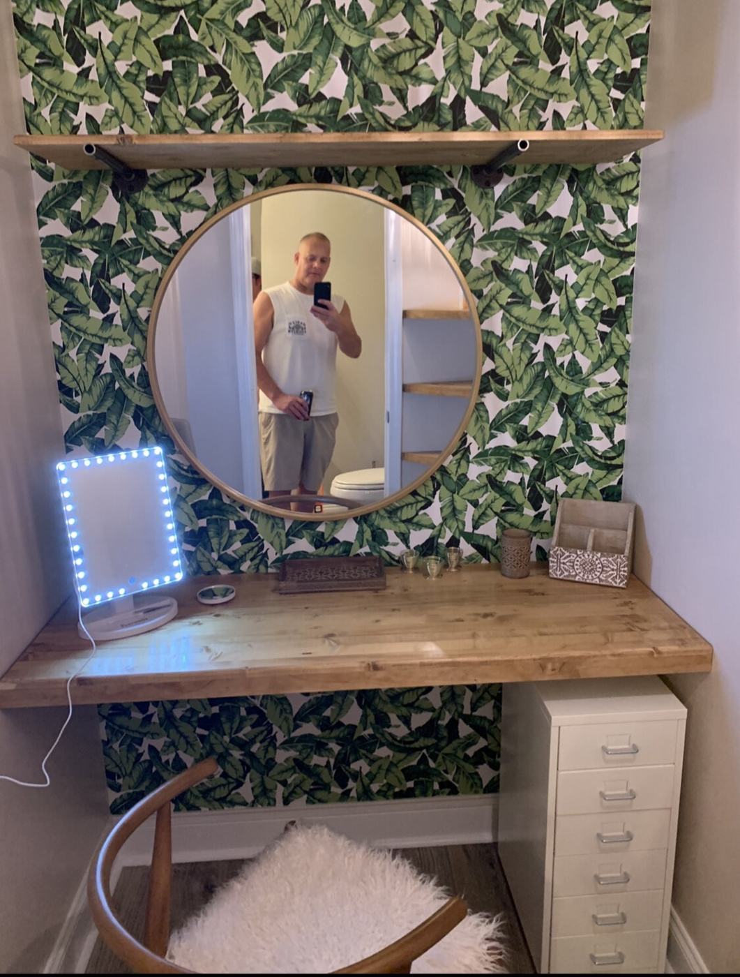 Built-in vanity desk with round mirror and floating shelf in a bedroom nook